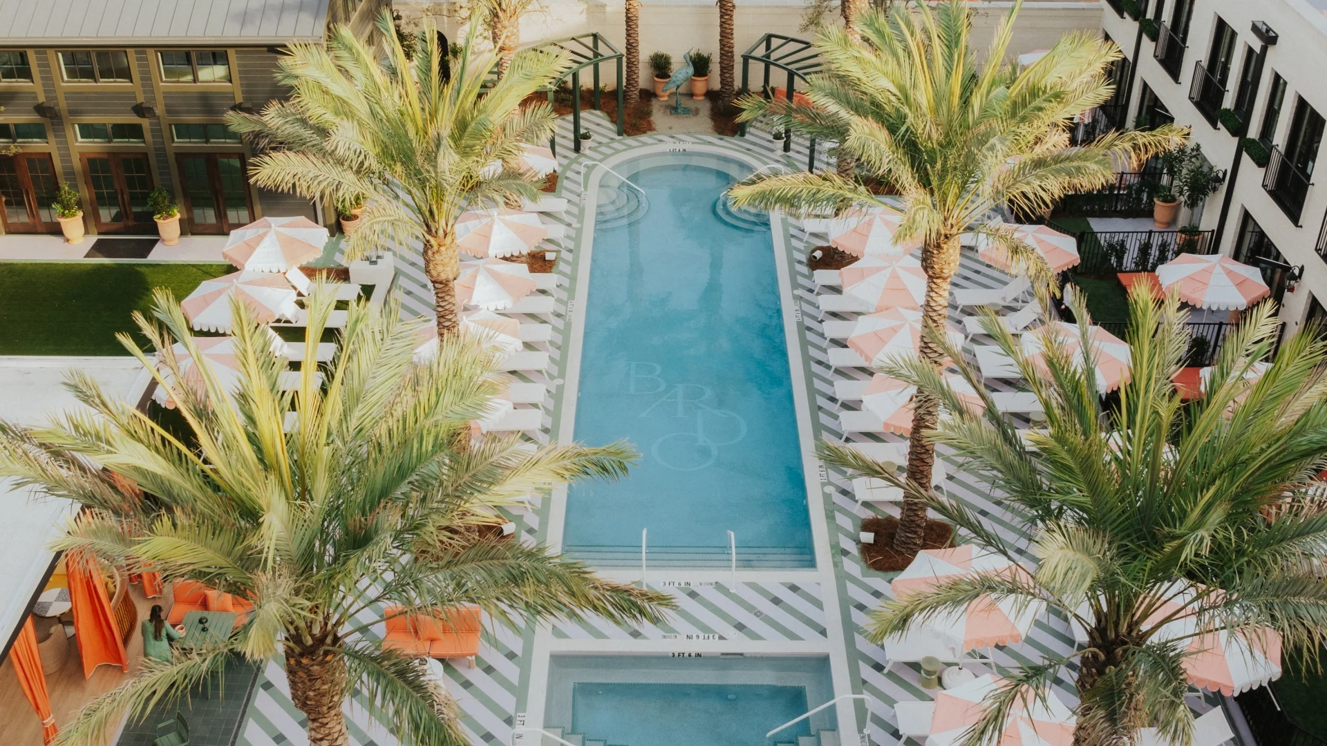 Aerial view of Hotel Bardo's palm-lined courtyard pool with striped loungers and scalloped umbrellas
